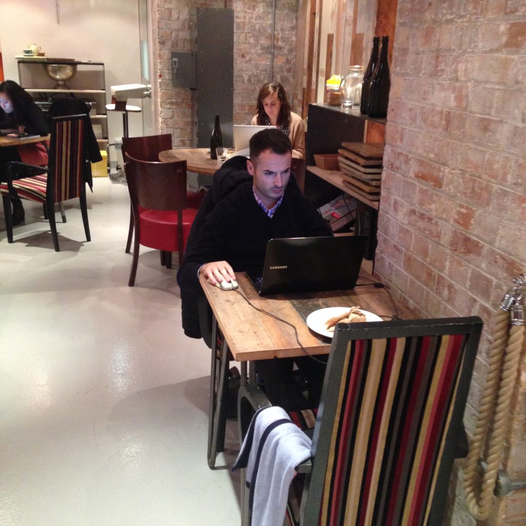 A table for two with one person working on a laptop, and a small table for four with one person working on a laptop.