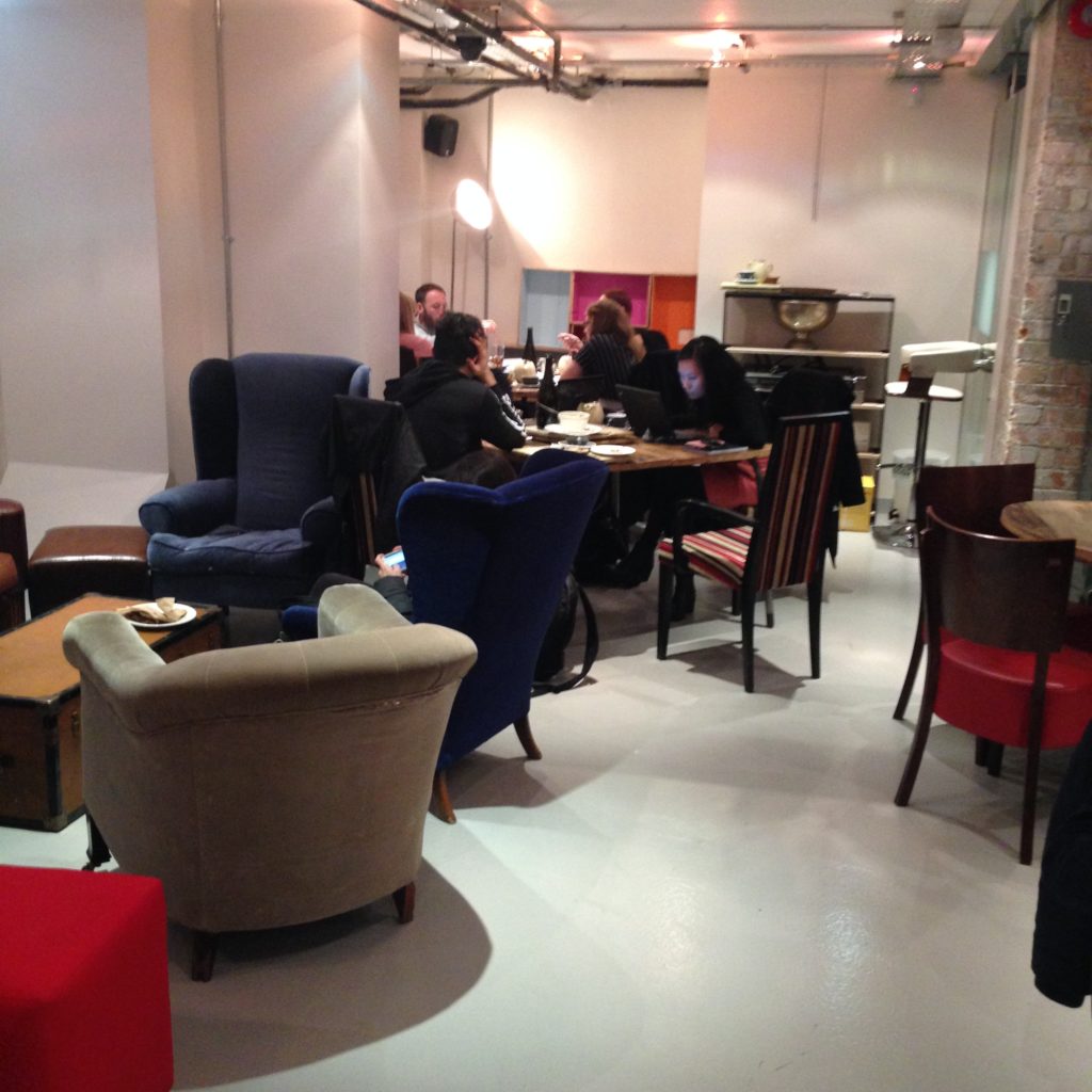 Assorted armchairs, and tables where two students sit together working quietly, and a group of four are collaborating.