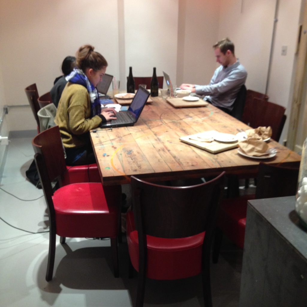 A communal table fowhere three people are working independently.